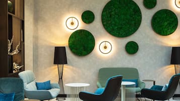 Una zona d'estar moderna amb un sofà, butaques, una taula rodona i un element decoratiu verd fixat a la paret.