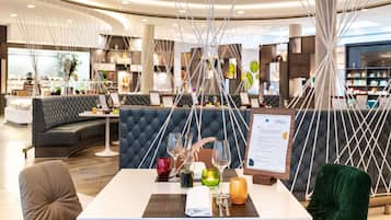 Ein modernes Restaurant mit einer gebogenen Sitzgruppe, einem Menüständer und Blick auf die Küche im Hintergrund.