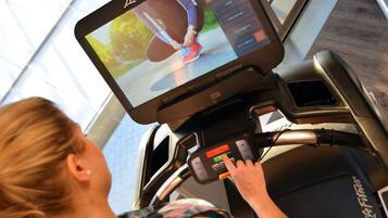 Una cinta de correr con pantalla digital que muestra a una persona corriendo, panel de control y el nombre de la marca 'Life Fitness'.
