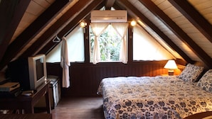 Un dormitorio acogedor en el ático con techo de madera, una cama con colcha floral, un escritorio con lámpara y una ventana con cortinas.