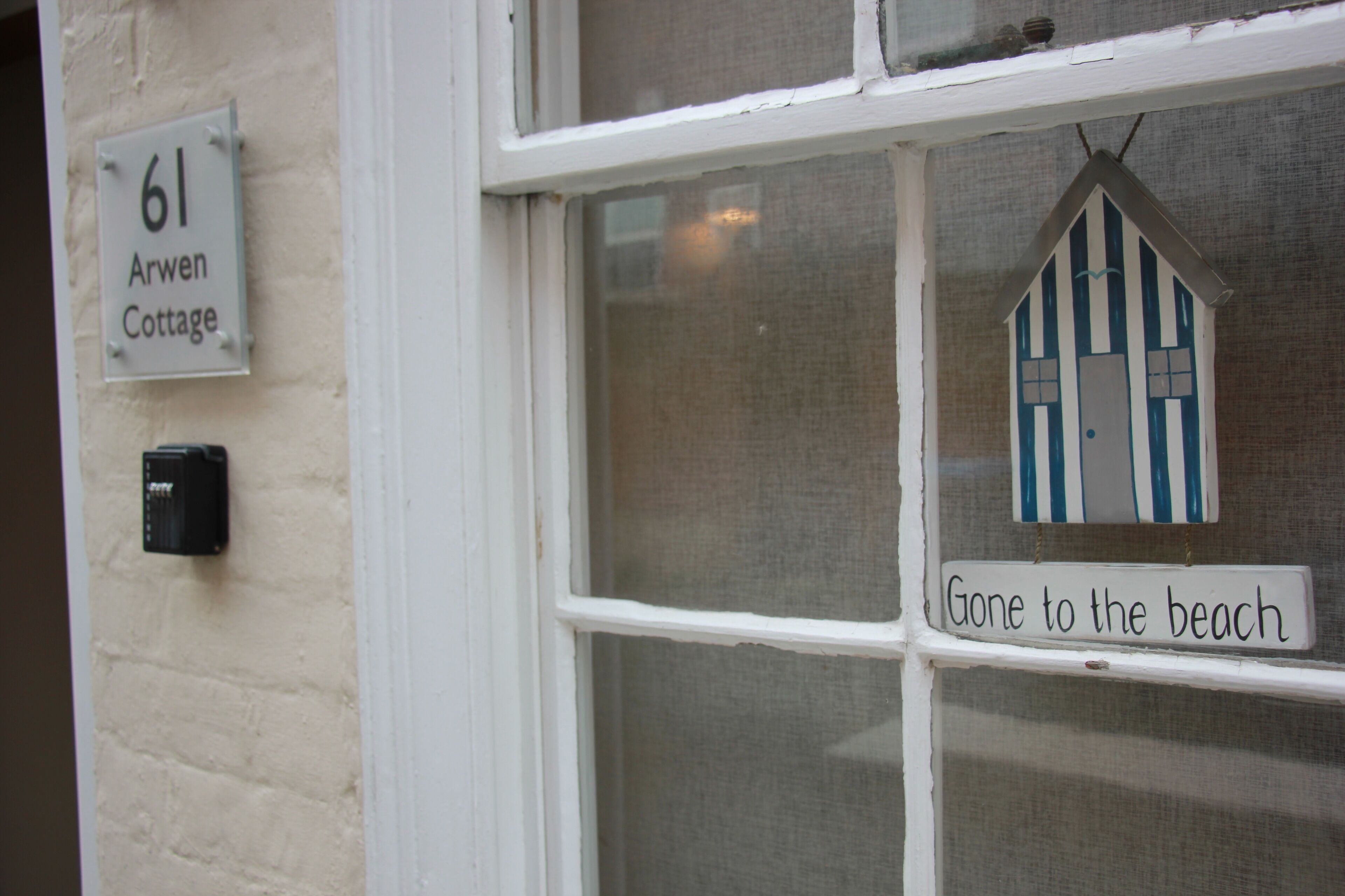 A window with a 'Gone to the beach' sign, a '61 Arwen Cottage' sign, and a small house decoration.