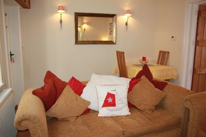 A cozy living room with a brown sofa, a white pillow with a red sailboat design, and two wall-mounted lamps.