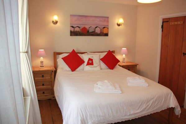 A neatly made bed with red pillows, a painting on the wall, and two bedside lamps.