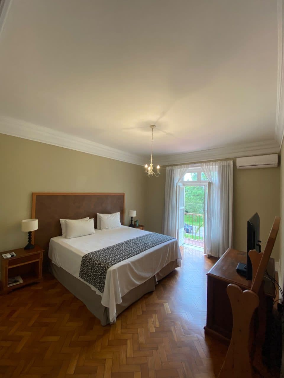 A hotel room with a large bed, a desk, a chair, a lamp, and a view of the outdoors.