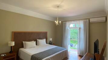 A hotel room with a large bed, a desk, a chair, a lamp, and a view of the outdoors.