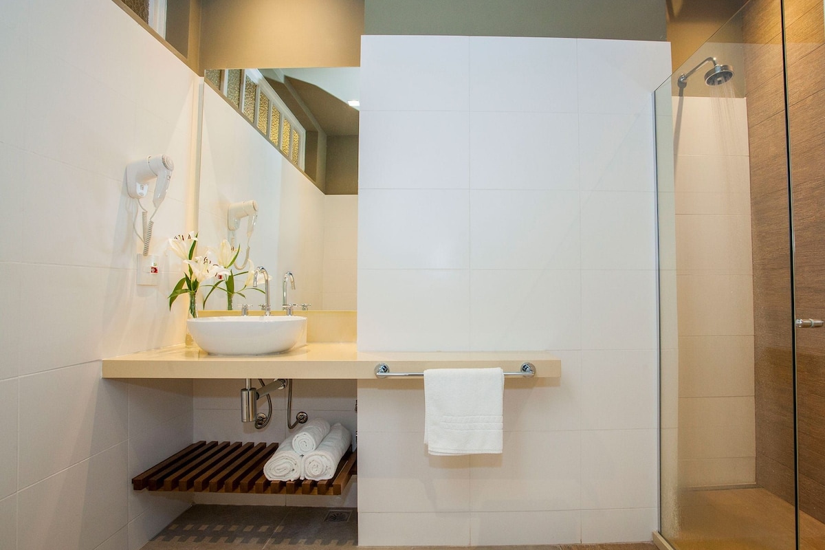 A modern bathroom with a large sink, a mirror, a towel rack, and a shower area.