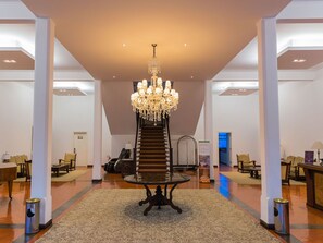 Eine geräumige Lobby mit einem prächtigen Kronleuchter, einer zentralen Treppe und Sitzbereichen.