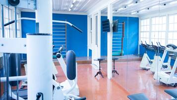 Un gimnasio con varias máquinas de ejercicio, un espejo grande y una pared azul brillante.