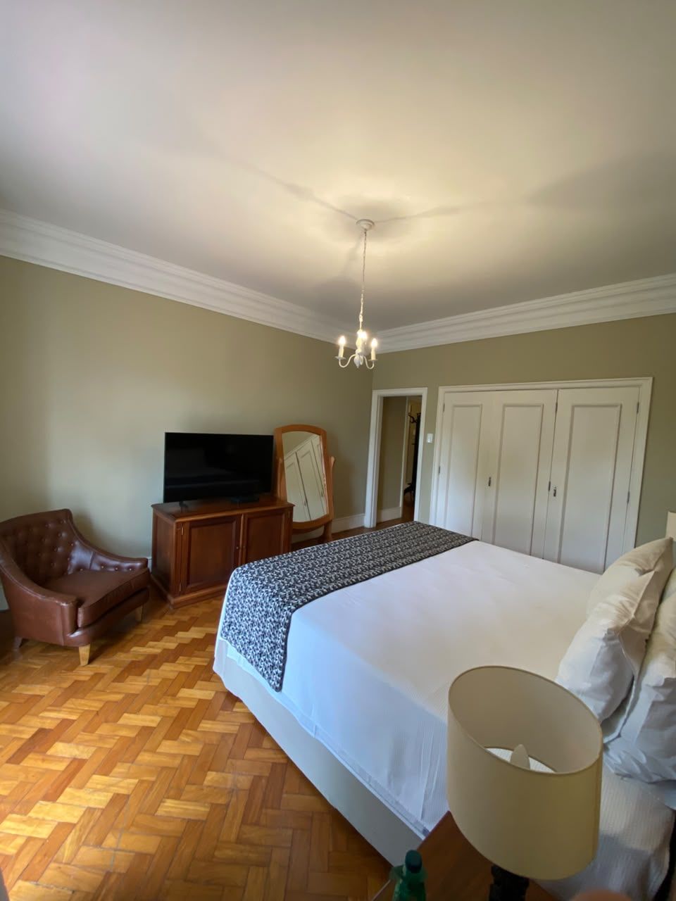 A bedroom with a large bed, a television, a wardrobe, and a chair.
