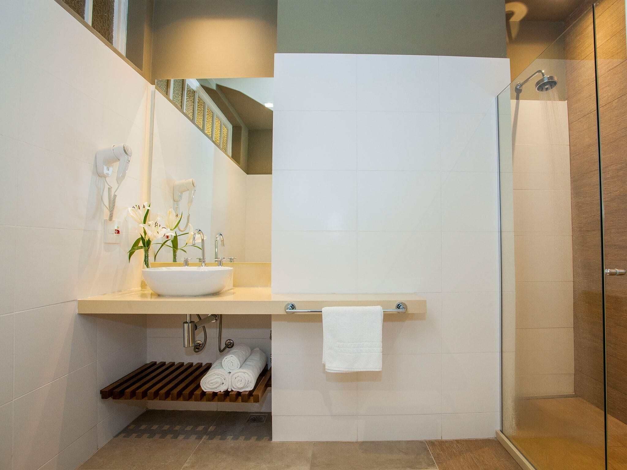 A modern bathroom with a large sink, a mirror, a towel rack, and a shower area.