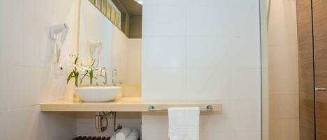 A modern bathroom with a large sink, a mirror, a towel rack, and a shower area.