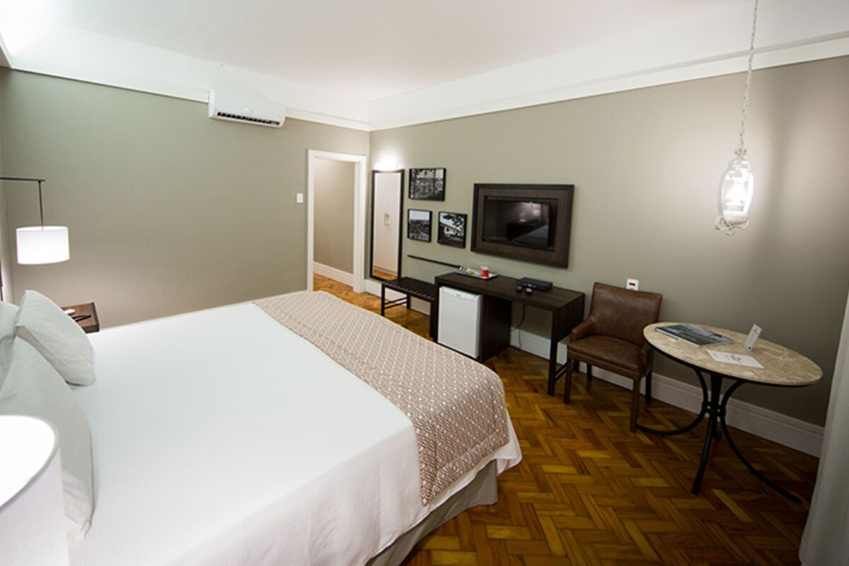 A hotel room with a bed, desk, chair, television, and a small table.