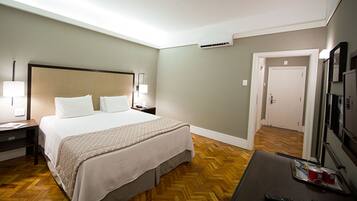 Una habitación de hotel con una cama grande, lámparas de noche, un escritorio con un control remoto y un equipo de aire acondicionado.