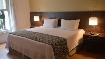 A hotel room with a large bed, two bedside lamps, a nightstand with a phone and remote, and a window with curtains.