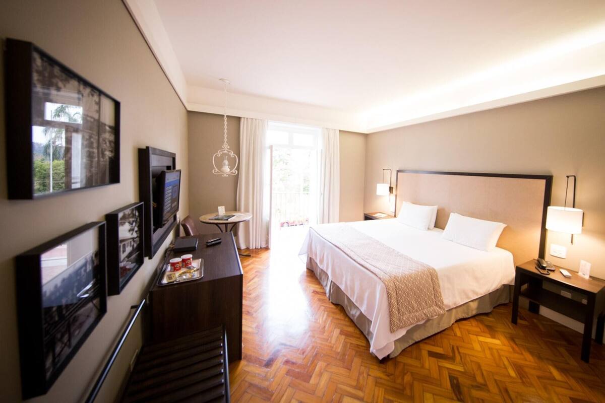 Une chambre d’hôtel comprenant un lit, des tables de chevet, un bureau avec une chaise, une télévision et des tableaux encadrés au mur.