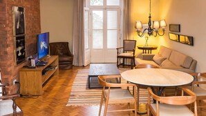 A cozy living room with a brick wall, a TV, a sofa, a dining table, and a chandelier. - Hotel Escola Bela Vista (Volta Redonda)