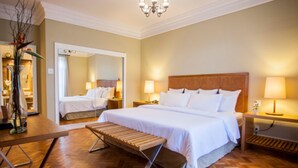 A hotel room with a large bed, two bedside tables with lamps, a wooden bench, a mirror, and a chandelier. - Hotel Escola Bela Vista (Volta Redonda)