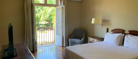Habitación de hotel con cama, escritorio, silla, lámpara y vista a zonas verdes por la ventana.