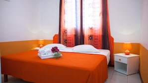 A hotel room with two beds, orange bedding, a nightstand with a lamp, and a window with curtains. - Etal Paradise, a Tropical Paradise in Sainte-Anne in Guadeloupe (SAINTE  ANNE)