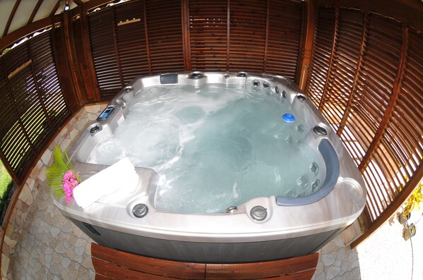 A hot tub with a stone surround, wooden slats, and a pink flower decoration.