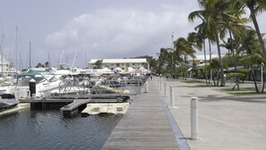 A marina with boats docked, a pedestrian walkway, and palm trees. - Etal Paradise, a Tropical Paradise in Sainte-Anne in Guadeloupe (SAINTE  ANNE)