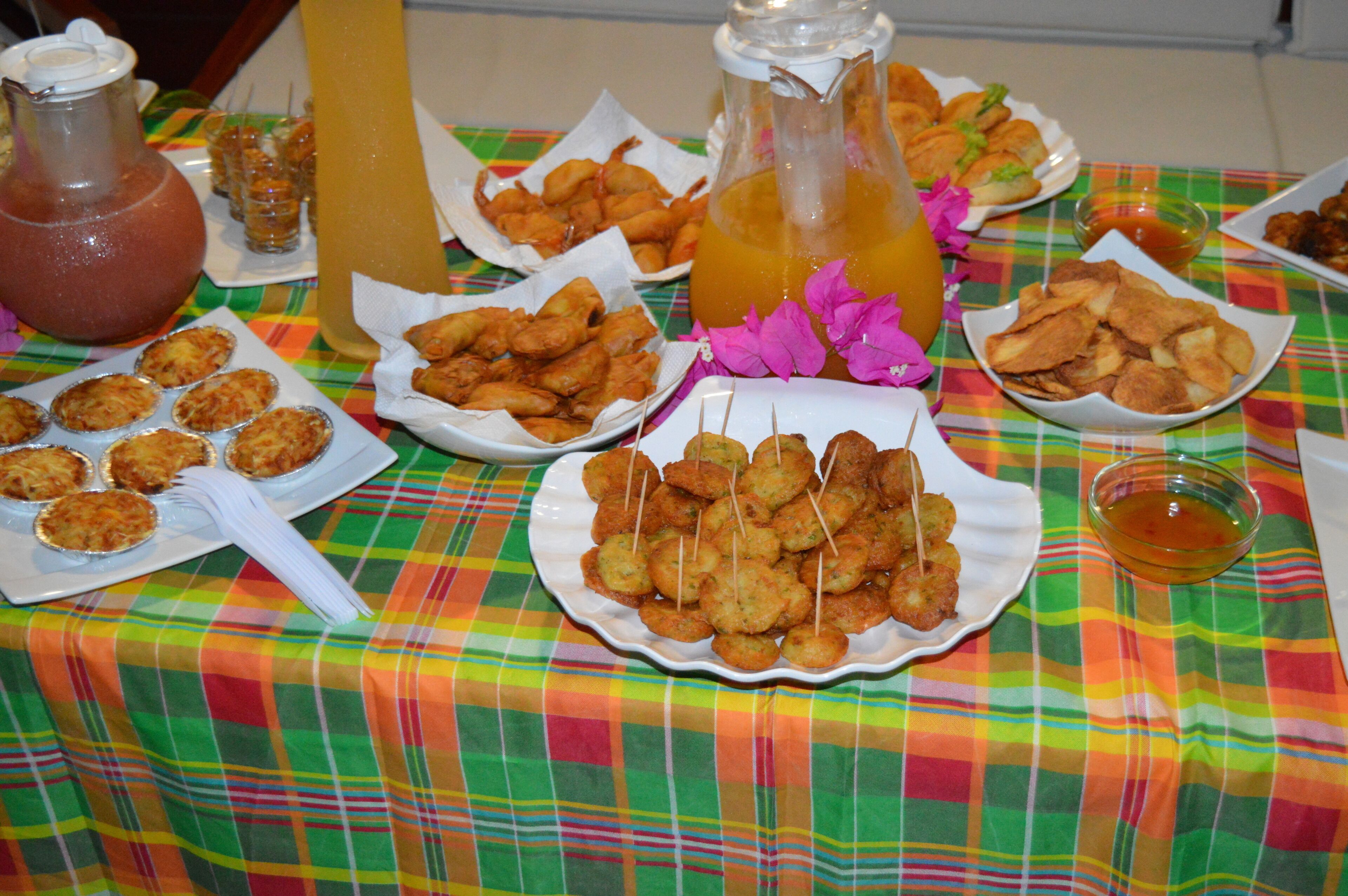 Een tafel met verschillende gerechten en drankjes, waaronder borden met gefrituurd snacken, een karaf sap en een fles saus.
