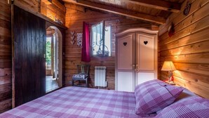 Quarto de cabana de madeira com cama, cômoda e janela com cortinas.