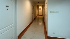 A corridor with white tiled floors and walls, a door labeled "205", and a fire alarm on the right wall. - The 1 Place Khonkaen (Khon Kaen)