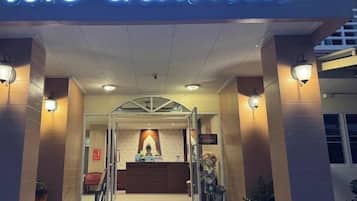 A hotel entrance with a reception desk, a staircase, and a sign with illuminated text.