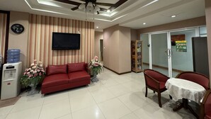 A hotel lobby with a red sofa, a dining table with chairs, a ceiling fan, a flat-screen TV, a water dispenser, and a refrigerator. - The 1 Place Khonkaen (Khon Kaen)