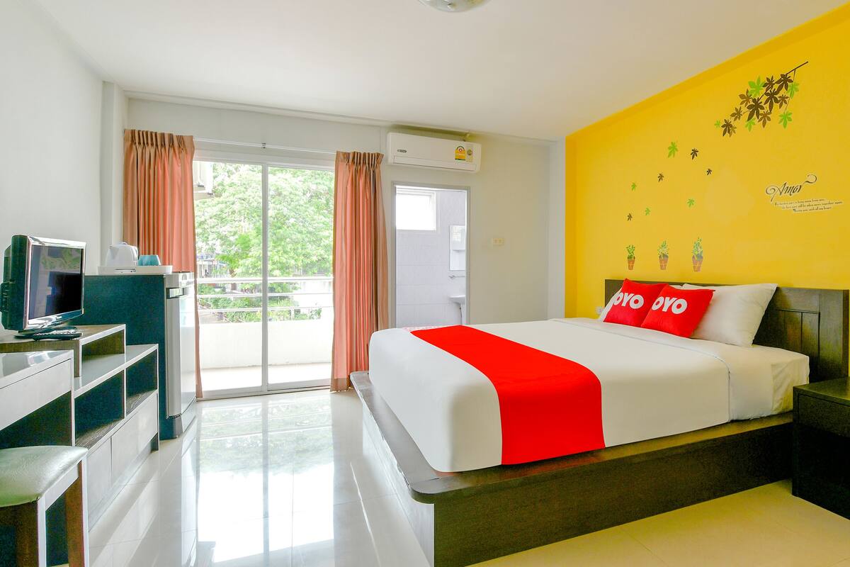 A hotel room with a bed, a TV, a desk, and a balcony with curtains.