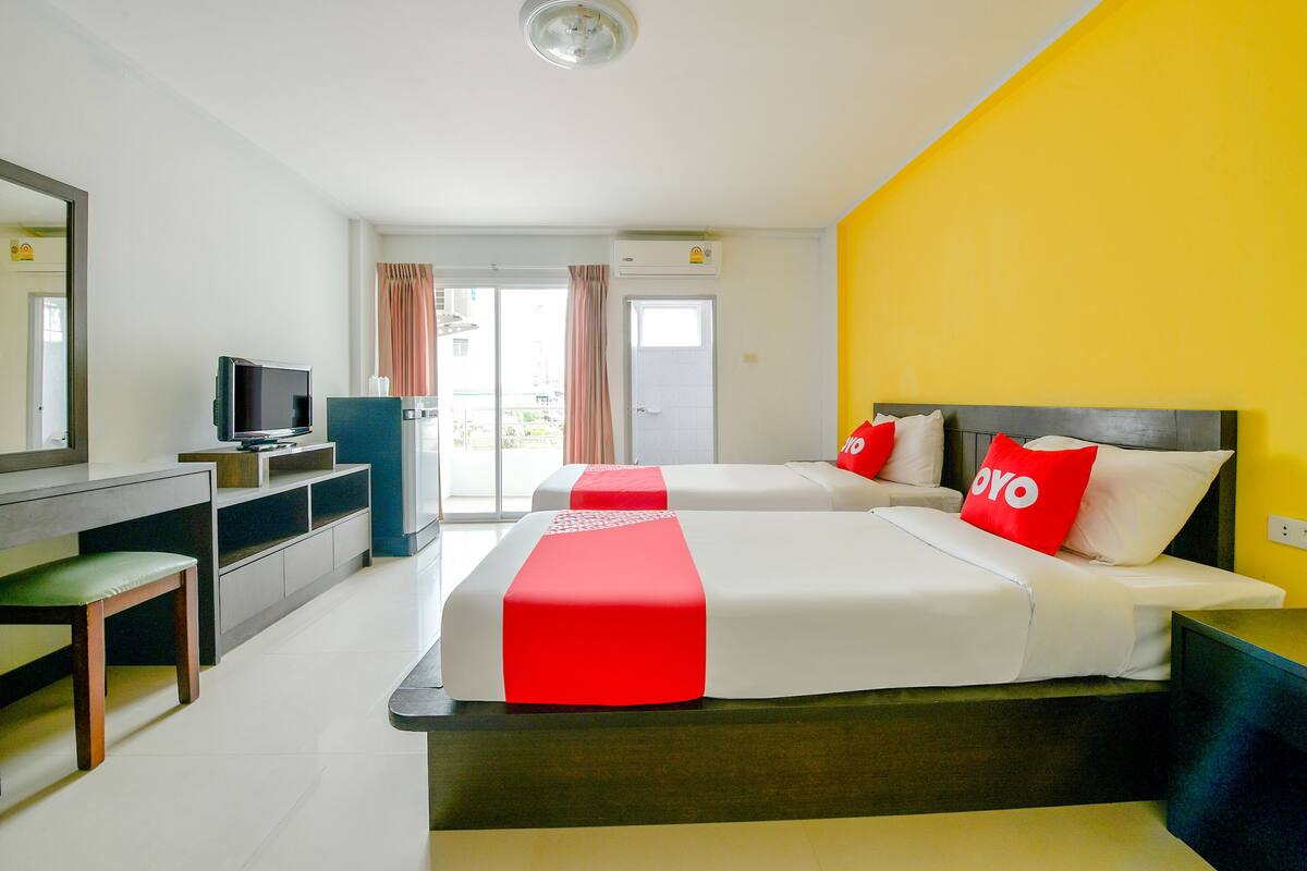 A hotel room with two beds, a desk with a television, and a view of the outside.