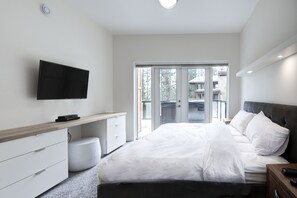 A modern bedroom with a large bed, a flat-screen TV mounted on the wall, and a sliding glass door leading to an outdoor balcony. - Just completed 4 bedroom, 5 bathroom modern Town home, pool table, sleeps 10 (Golden)