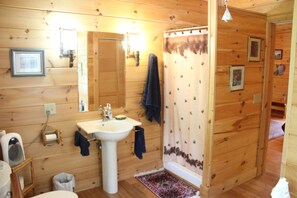 Casa de banho de cabana de madeira, com lavatório, espelho e cortina de chuveiro.