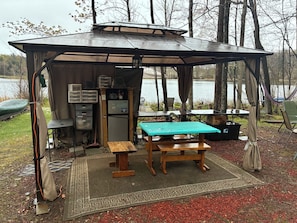 A covered outdoor area with a table, chairs, a refrigerator, and a small kitchen setup.
