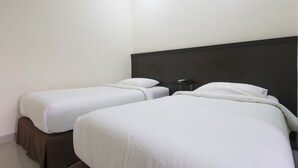 Une chambre d’hôtel avec deux lits simples, une tête de lit sombre et une petite table de chevet.
