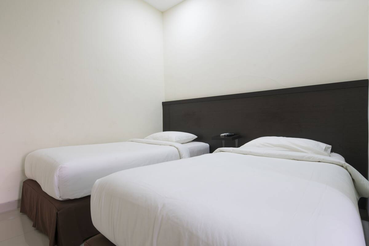A hotel room with two single beds, a dark headboard, and a small bedside table.