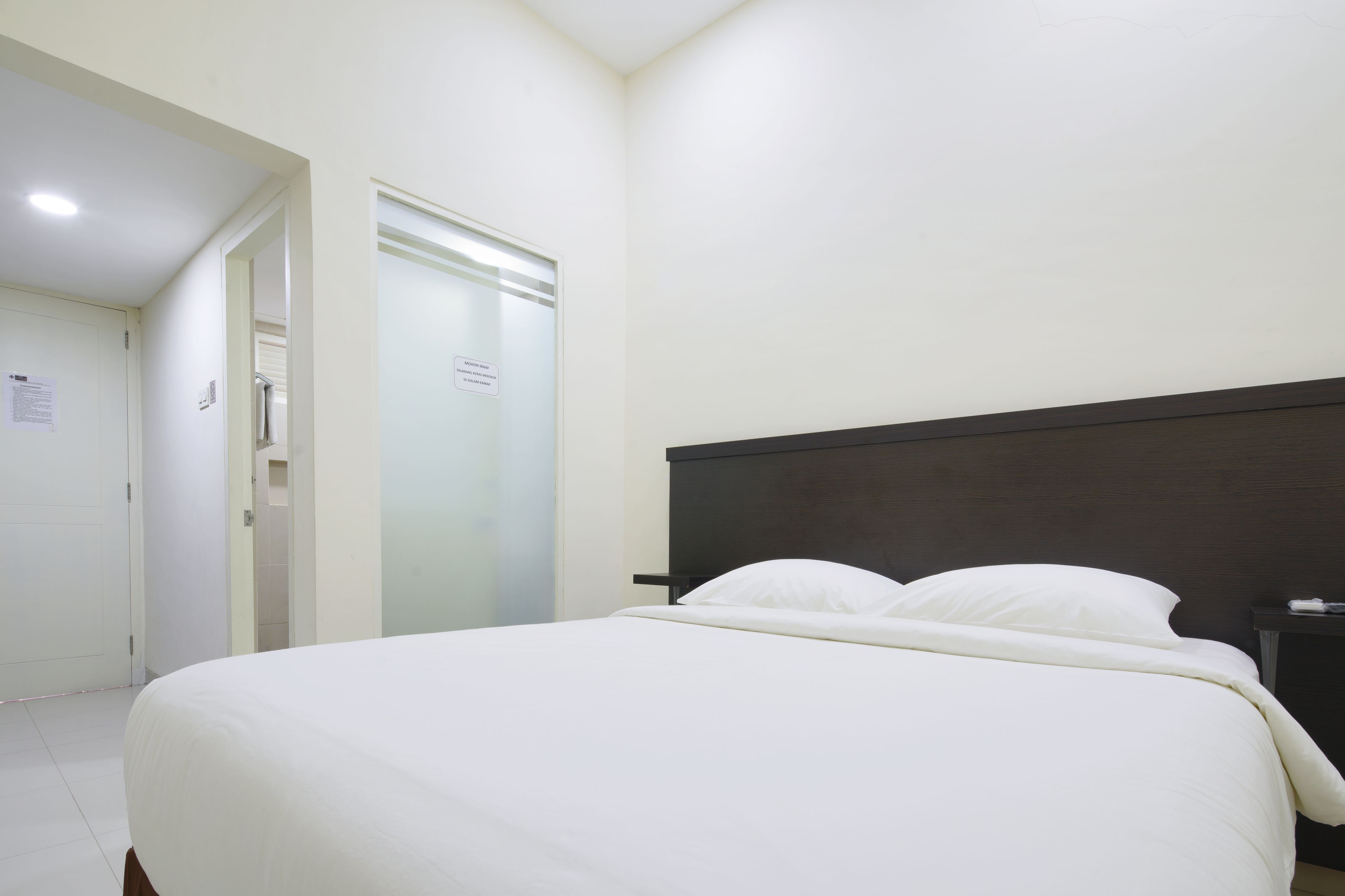 Una habitación de hotel con una cama, una mesita de noche, una puerta y una pared con un cartel.