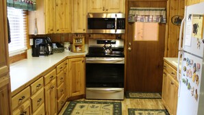 A compact kitchen with wooden cabinets, a stove, microwave, and refrigerator. - Gateway To Yellowstone Park And Outdoor Adventure. FREE internet and cleaning. (Island Park)