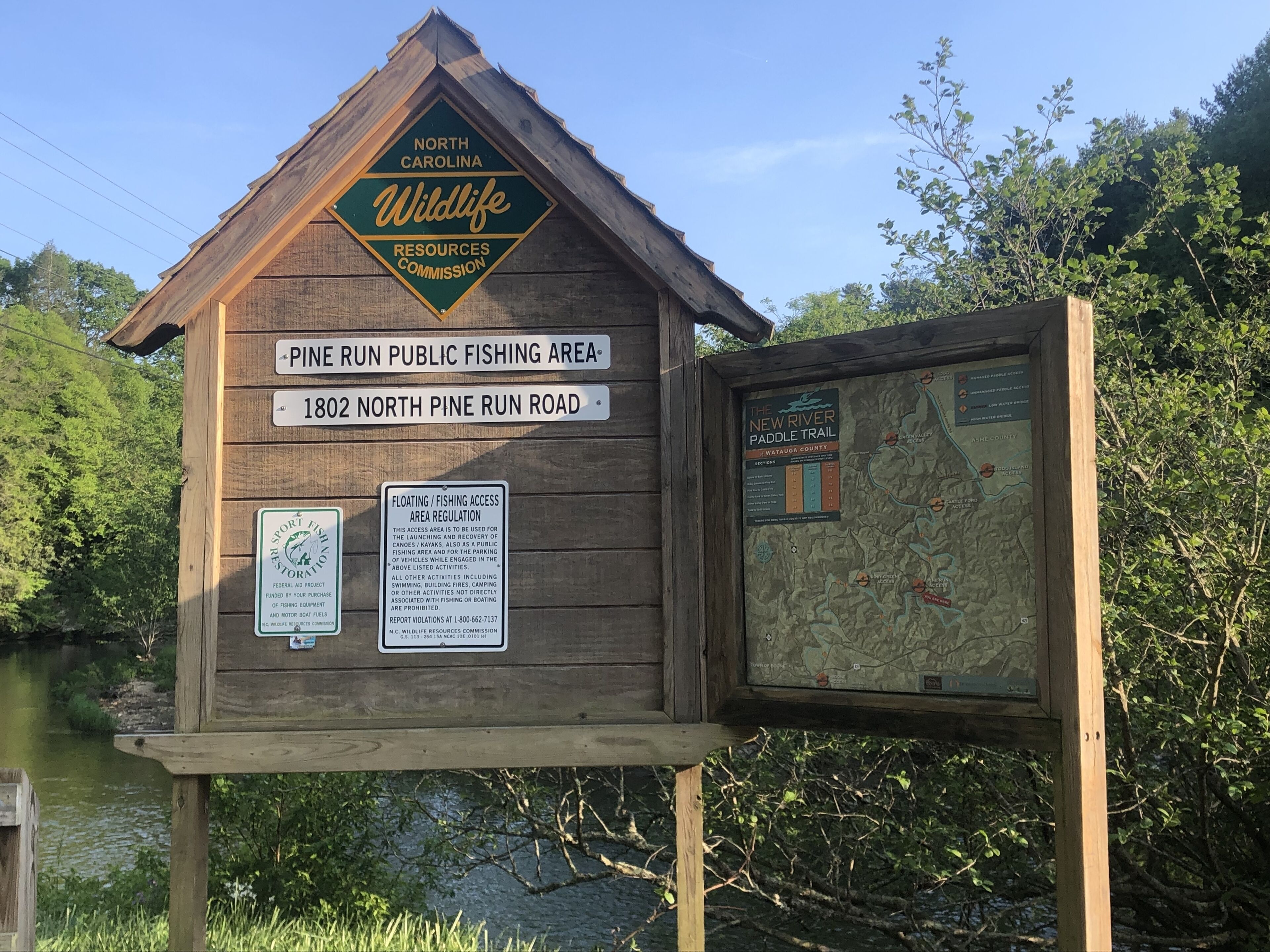 A wooden signboard with multiple informational signs, including a map and a notice about the Pine Run Public Fishing Area.