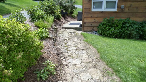 Un sendero de piedra que conduce a una casa de madera con una ventana.