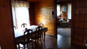 Un interior de madera con una mesa de comedor y sillas, una lámpara, y un sofá en la habitación contigua.