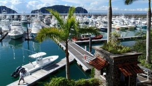 A marina with numerous boats docked, a dock with a person walking, and palm trees. - Luxury Los Sueños Condo - Marina, Pools & Golf. Fishermans Paradise! (Los Suenos)