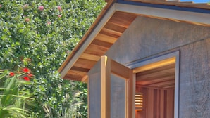 Un sauna avec une structure extérieure en bois, une porte et un petit banc en bois à l’intérieur.