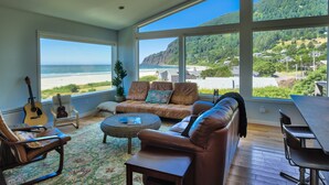 Un salon spacieux doté d’une grande fenêtre offrant une vue sur la plage et les montagnes.