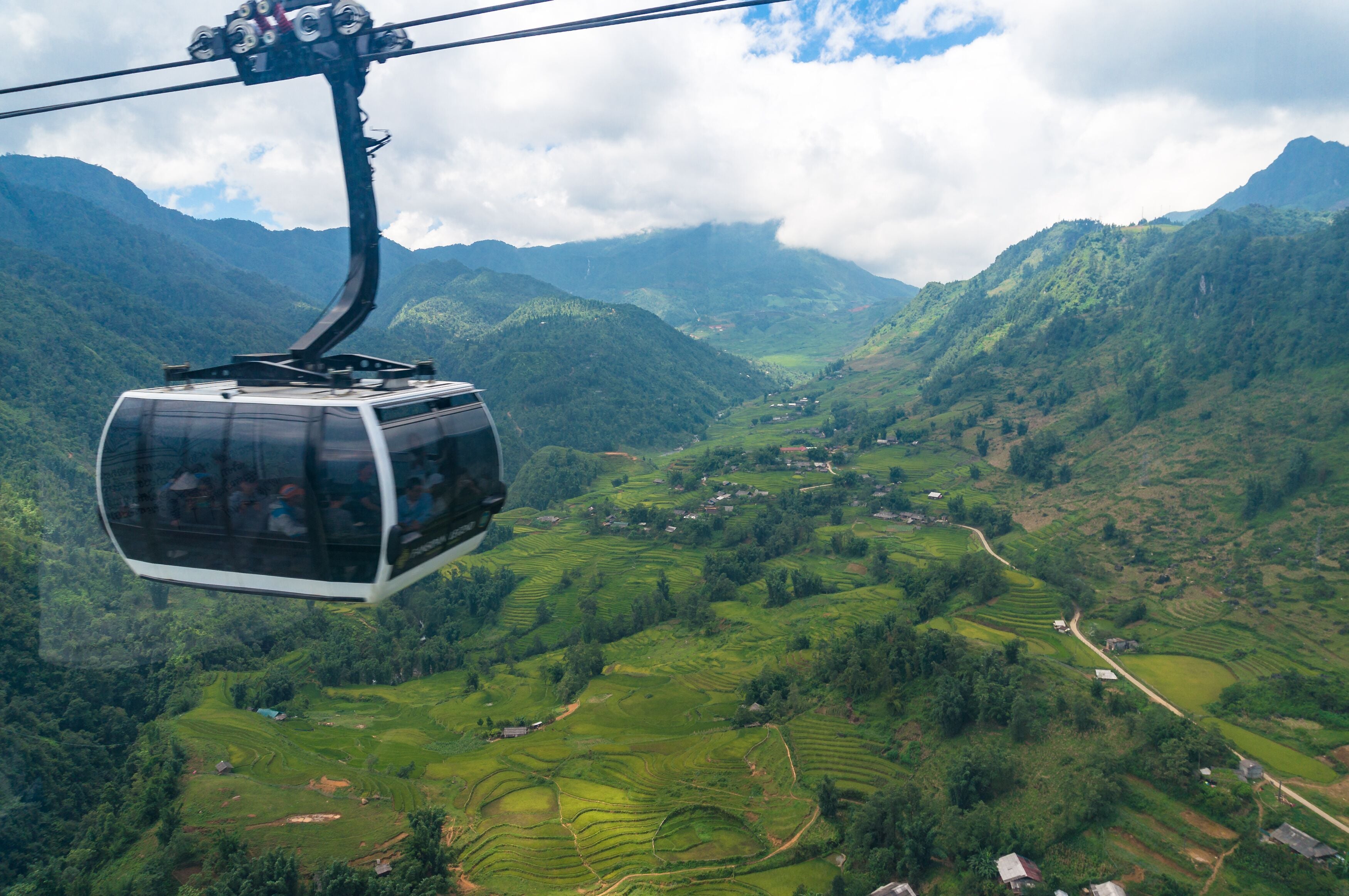Un teleférico sobre campos escalonados con montañas al fondo.