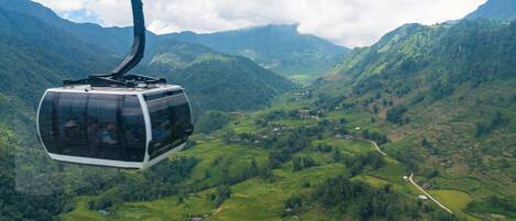 Un teleférico sobre campos escalonados con montañas al fondo.