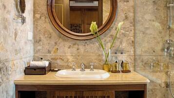 A bathroom with a marble wall, a wooden vanity, a round mirror, and a shower area.