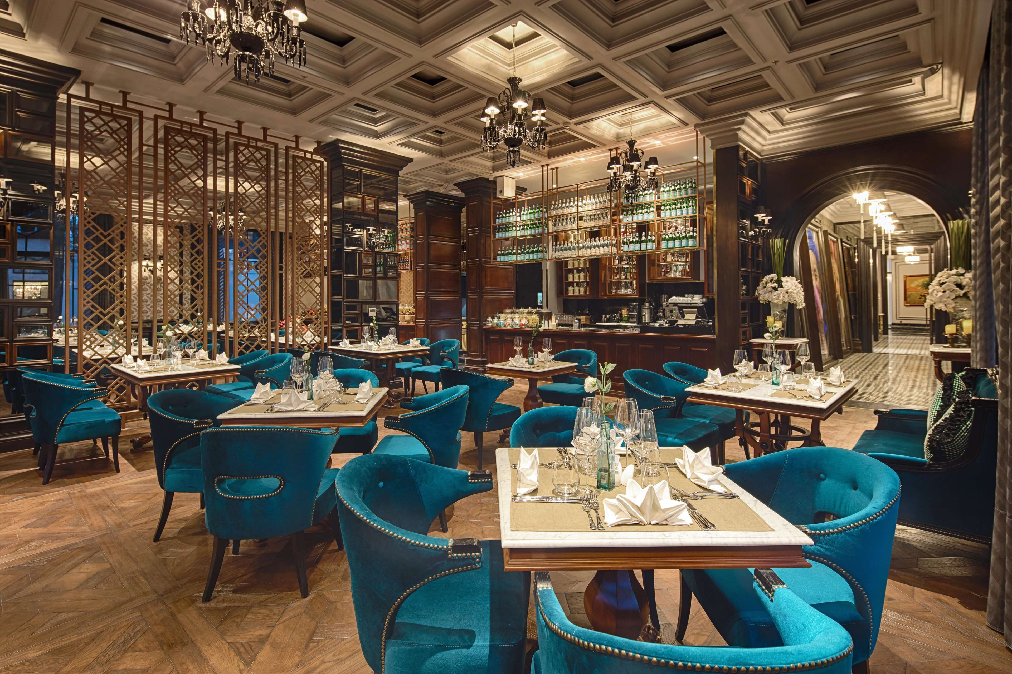 Un restaurant avec des chaises à revêtement bleu, des tables en bois et un bar avec des étagères remplies de bouteilles.