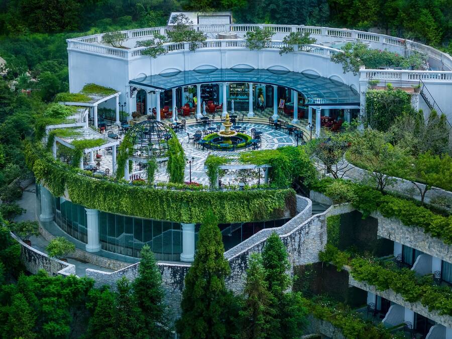 A large, white building with a central courtyard, surrounded by lush greenery and stone walls.
